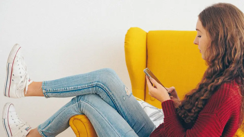 woman in red sweater and blue denim jeans sitting on yellow couch