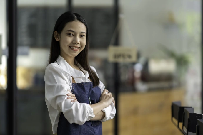 De lachende eigenaar stond met zijn armen over elkaar en een blauw schort om bij de ingang van het café.