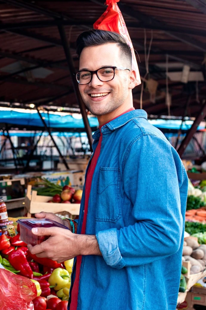 Portrait of young man standing in front of a vegetable counter in an outdoor market.