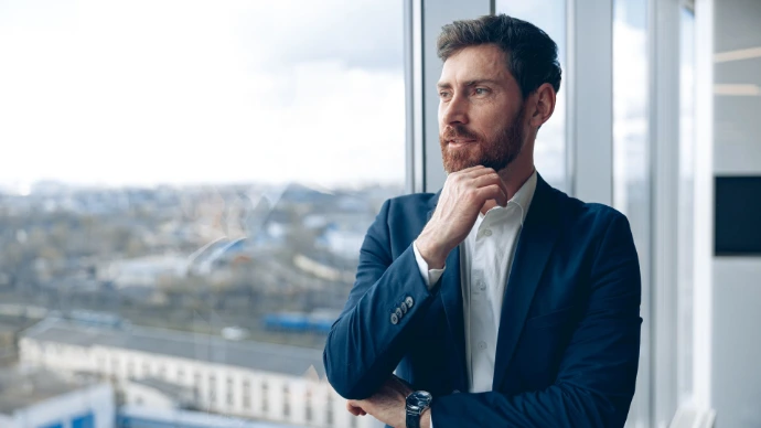 Focused attractive businessman looking out the window standing in a modern office