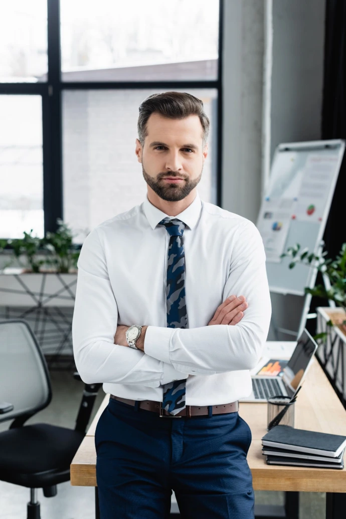 economist in white shirt standing in office with crossed arms and looking at camera