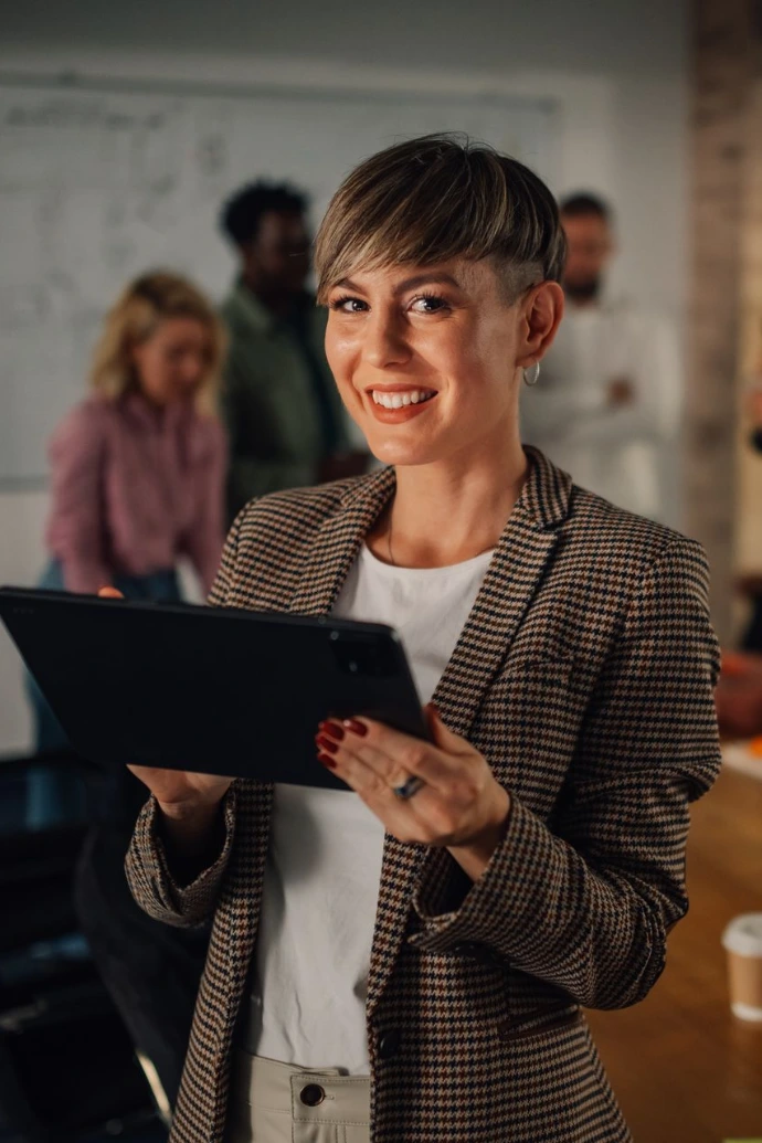 Smiling businesswoman holding tablet, leading meeting in modern office