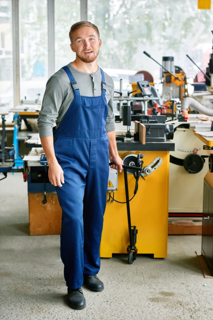 Man Wearing Blue Overalls in Workshop with Machinery